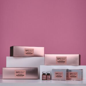 A display of GFCell product packaging and vials on a white surface against a pink background. The setup includes multiple rose-gold boxes labeled "GFCell" with variants such as "Eco Hyal" and "Eco Hyal N," alongside two small amber vials with white caps, suggesting a premium skincare or health supplement line.